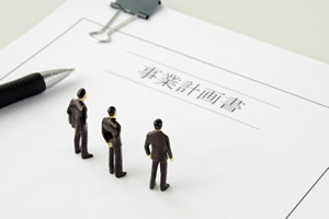 事業計画書の上にペンと小さな3人のスーツの男性が立っている画像